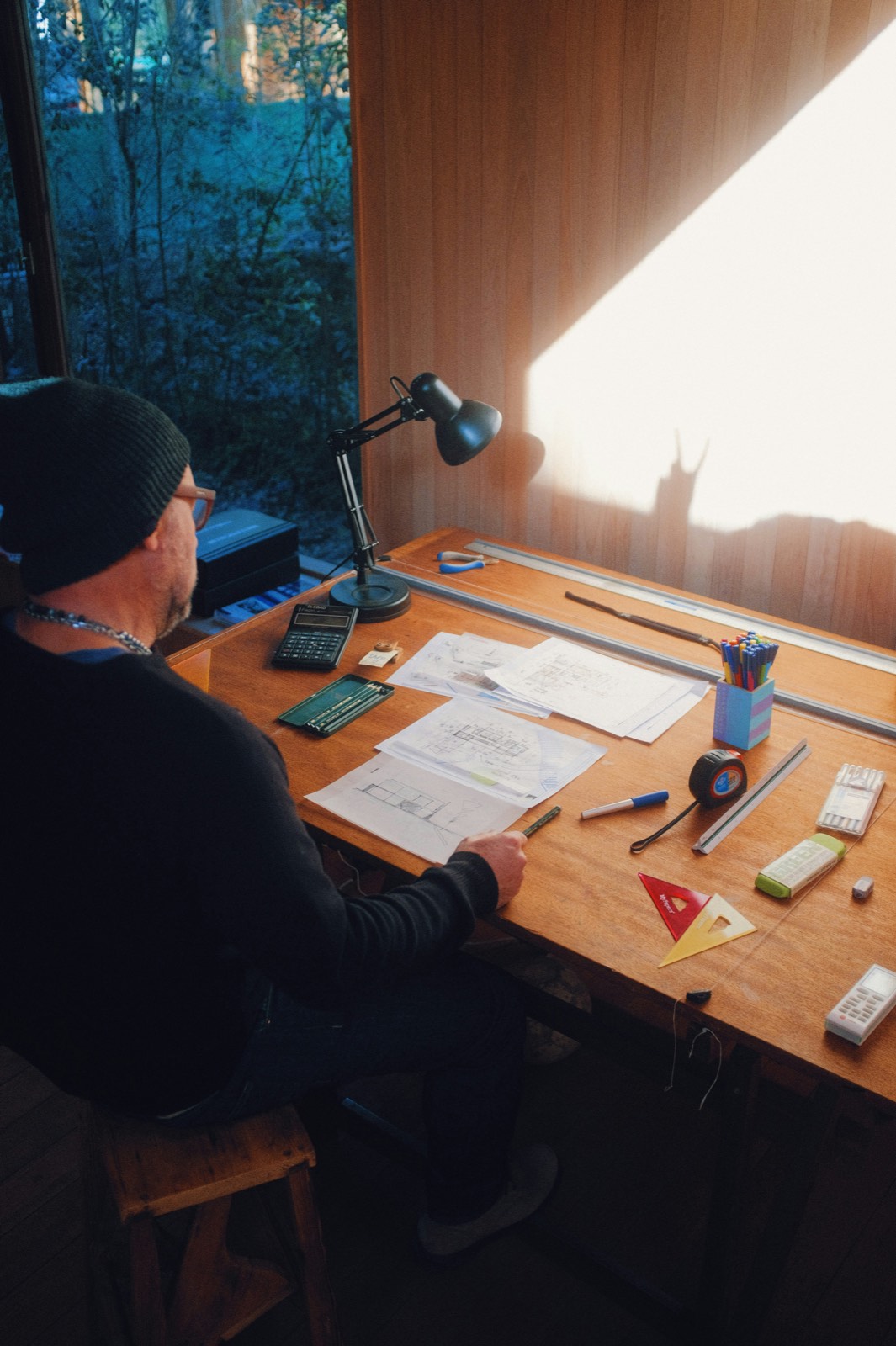 Person drawing plans at a wood desk