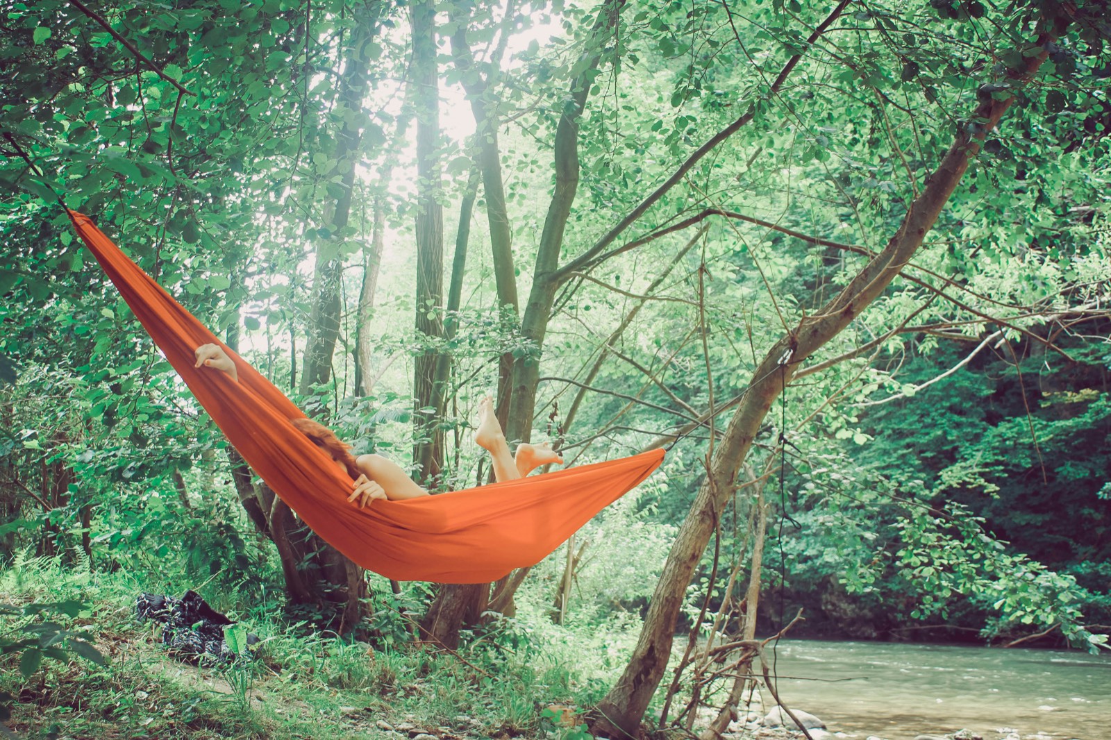 Person in an orange hammock by a river