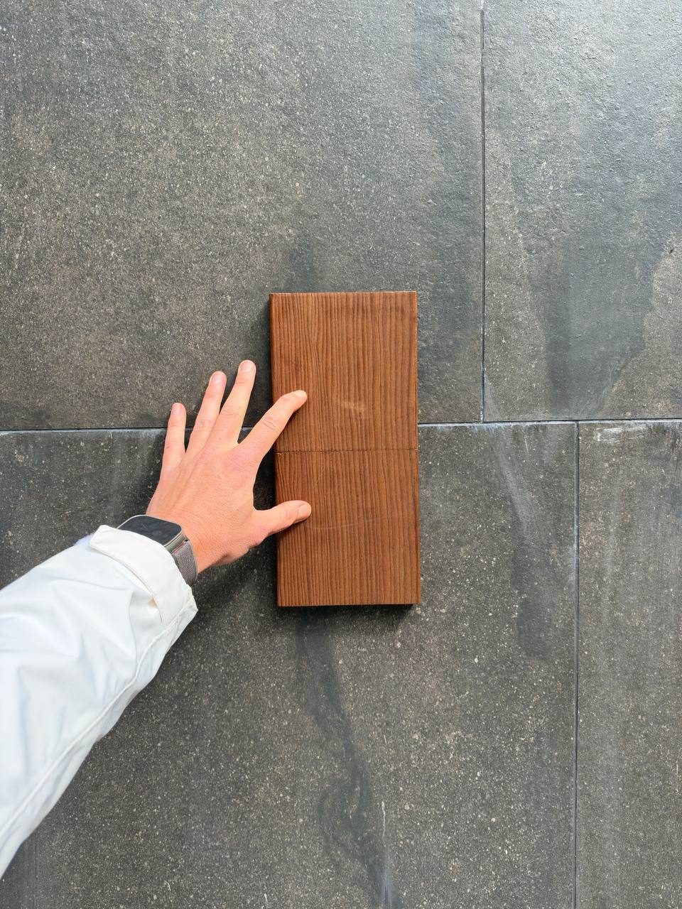 Wood sample held against dark stone tile