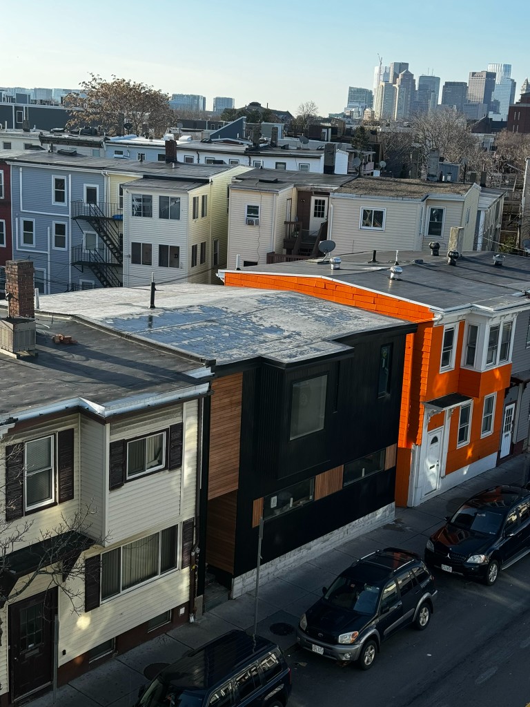 The house from above, black metal beside the orange neighbor, Boston skyline beyond